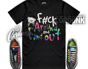 Peut inclure: T-shirt noir avec l'inscription "F#ck Around and Find Out" en lettres colorées et un motif d'ours en peluche. L'image comprend également une paire de baskets noires et grises avec des lacets colorés.