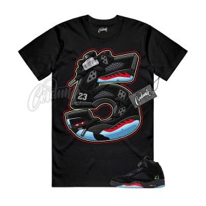 May include: A black short-sleeve t-shirt featuring a large graphic of the number five shaped like a black sneaker with red accents, light blue soles, and the number 23. The shirt includes the text Cordunk on the neck and a hanging tag.