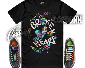 Peut inclure: T-shirt noir avec un motif coloré "Broken Heart" et le texte "Love Me Not Hurt Me". L'image comprend une paire de baskets grises et noires avec des lacets et des détails colorés. La marque "Cordunk" est également visible.