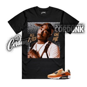May include: Black t-shirt featuring a portrait of Tupac Shakur with the text "ALL EYES ON ME." The shirt also displays the Cordunk logo and a pair of orange and tan sneakers.