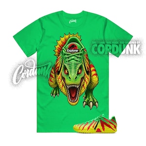 May include: Bright green t-shirt featuring a detailed illustration of a dinosaur with a sneaker design. The dinosaur graphic is green, yellow, and red. The word "Explorer" is visible on the sneaker. A matching sneaker is at the bottom of the image.