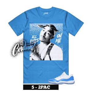 May include: A light blue t-shirt featuring a black and white image of a person with the text "ALL EYES ON ME". The shirt also has a white and blue sneaker at the bottom. The brand name "Cordum" is on the left side.