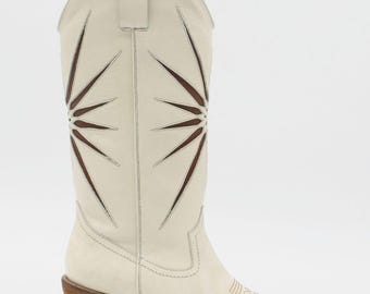Peut inclure: Botas de cowboy blanc cassé avec un bout pointu et un talon en bois. La botte présente un motif en forme d'éclat d'étoile avec des découpes marron et des coutures décoratives sur le bout. Le talon mesure environ 5 cm.