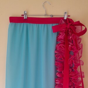 Può includere: Una gonna blu chiaro con un bordo di volant rosa e un nastro rosa legato in vita.