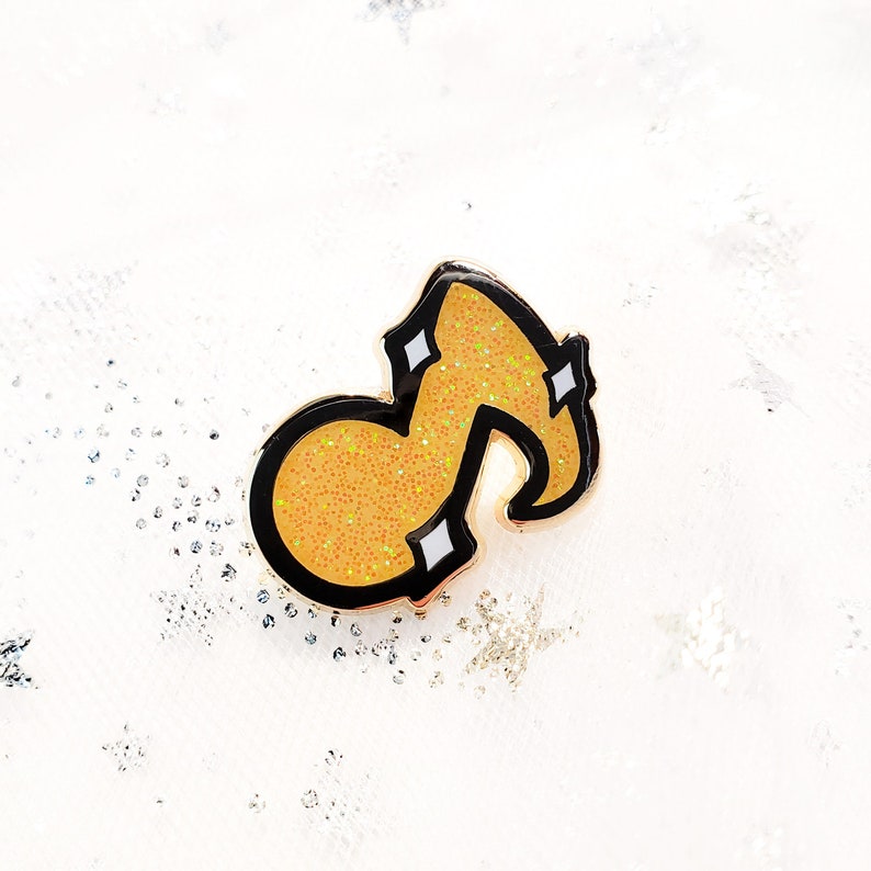 May include: A gold musical note pin with black outline and yellow glitter.