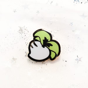 May include: A white and green enamel pin featuring a cartoon turnip with a green leafy top.