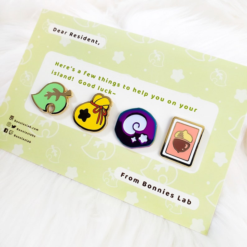 May include: A set of four gold-colored enamel pins featuring characters from the Animal Crossing video game series. The pins are on a card with the text "Dear Resident, Here's a few things to help you on your island! Good luck- From Bonnies Lab".