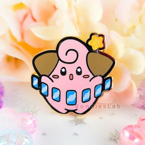 May include: A pink and gold enamel pin featuring a cartoon character with a curled tail, brown ears, and a blue and white striped collar. The character has a surprised expression with large eyes and an open mouth. The pin has a sparkly gold star on top.