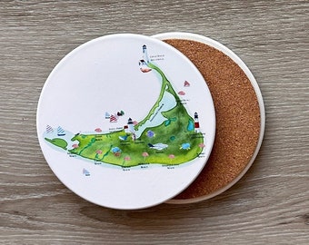 May include: A white ceramic coaster with a map of the island of Nantucket, Massachusetts. The map features various landmarks, including lighthouses, beaches, and towns. The coaster has a cork backing.
