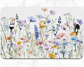 May include: A white placemat with a watercolor design of colorful wildflowers. The placemat features a variety of flowers in shades of blue, pink, yellow, and green.