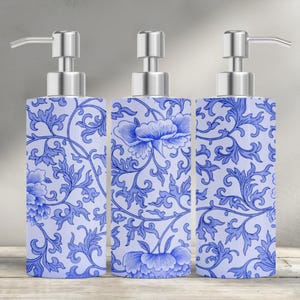 May include: Three ceramic soap dispensers with a blue and white floral pattern. Each dispenser has a silver pump and a rectangular shape. The floral design includes flowers and leaves.