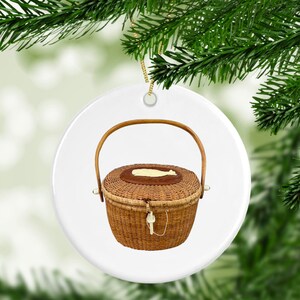 May include: A white ceramic Christmas ornament featuring a brown wicker basket with a wooden handle and a white whale design on the lid.