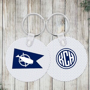 May include: Two round keychains with a white background and small navy blue polka dots. One keychain features a navy blue nautical pennant flag with a white whale and rope graphic. The other displays a navy blue circular monogram with the letters KCH.