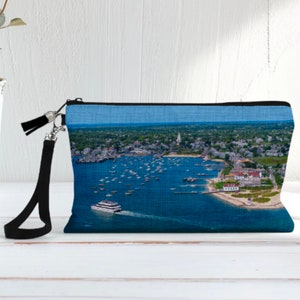 May include: A blue and black zippered pouch with a printed image of a coastal town and harbor with boats. The pouch has a black strap.
