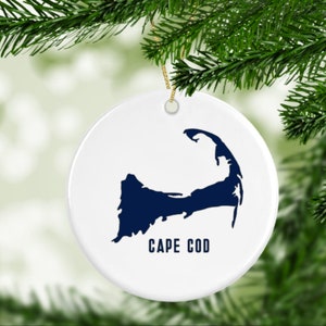 May include: White ceramic Christmas ornament with a blue silhouette of Cape Cod and the text "CAPE COD" printed below.