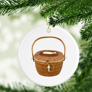 May include: A round white ceramic ornament with a brown wicker basket with a handle and a white lid. The basket has a brown leather-like trim around the lid.
