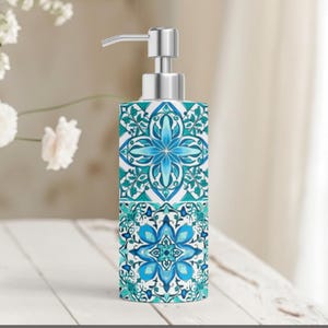 May include: A decorative soap dispenser with a floral tile design in shades of teal and white. The dispenser has a silver pump and a rectangular shape, perfect for a bathroom or kitchen. The design features symmetrical floral patterns.