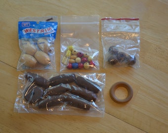 May include: Four bags of wooden beads, one bag of colorful beads, and a wooden ring. The bags are clear plastic with a zipper closure. The beads are various shapes and sizes. The ring is brown and has a smooth finish.