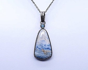 May include: A silver chain necklace with a pendant featuring a blue and white agate stone set in silver. The pendant is teardrop shaped and has a small blue gemstone at the top.