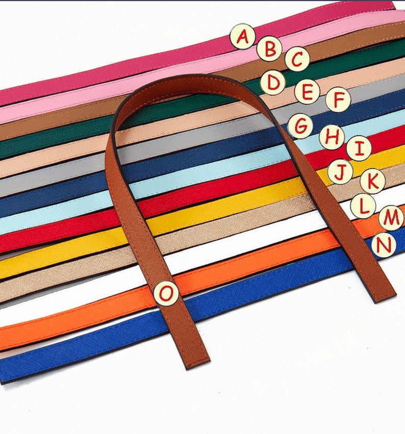 Puede incluir: Un conjunto de 15 correas de cuero de colores con un asa de cuero marr&oacute;n. Las correas est&aacute;n dispuestas en un patr&oacute;n de arco&iacute;ris y est&aacute;n etiquetadas con las letras de la A a la O.