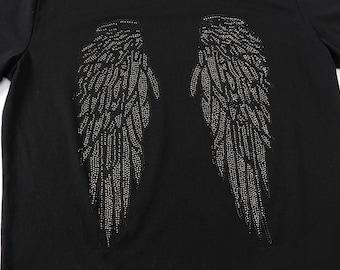 Puede incluir: Camiseta negra con un diseño de alas de ángel de pedrería plateada en la espalda.