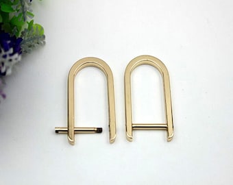 May include: Two gold-toned metal D-rings with a straight bar across the top. The rings are about 2 inches in diameter.