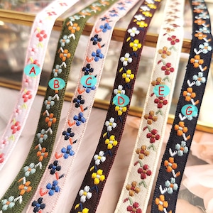 Könnte beinhalten: Sortiment aus sechs floral gemusterten Bandborten in verschiedenen Farben, darunter rosa, grün, blau, braun, beige und schwarz. Die Bänder zeigen ein sich wiederholendes Muster aus kleinen Blumen.