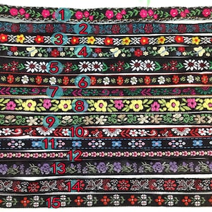 May include: Fifteen decorative ribbons with floral and geometric designs. The ribbons display colours such as pink, yellow, white, and blue, set against a black backdrop. Each ribbon has a unique pattern, ideal for crafts and embellishments.