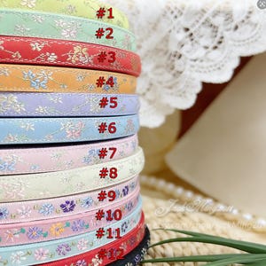 Könnte beinhalten: Ein Stapel bunter Stirnbänder mit floralen Mustern. Die Stirnbänder sind in verschiedenen Farben erhältlich, darunter Grün, Rot, Orange, Blau und Rosa. Jedes Stirnband ist mit einer Nummer von #1 bis #12 versehen.
