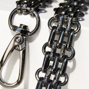 May include: A black metal chain with a decorative design and a silver swivel clasp. The chain is made of interlocking links and has a polished finish.