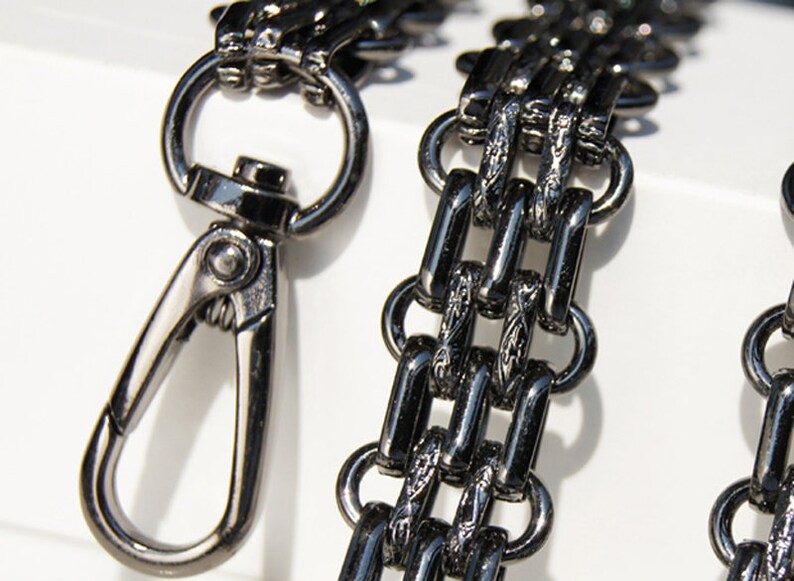May include: A black metal chain with a decorative design and a silver swivel clasp. The chain is made of interlocking links and has a polished finish.