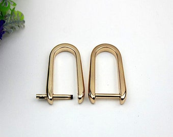 May include: Two gold-toned metal D-rings with a swivel bar connector. The rings are about 2 inches in diameter.