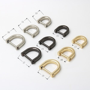 Op de afbeelding: Zes D-vormige metalen ringen in verschillende maten en afwerkingen. De ringen zijn zilver, goud en zwart. De ringen worden gemeten in inches.