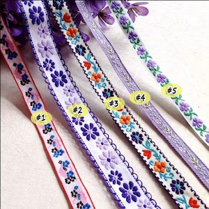 以下が含まれることがあります： 花柄の刺繍が施された、紫と白の異なるリボン5種類。リボンは#1から#5まで番号が付けられています。