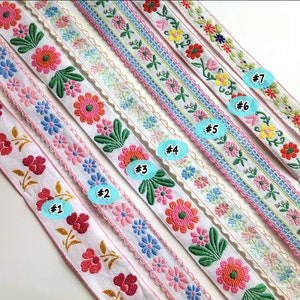 Könnte beinhalten: Sieben verschiedene weiße bestickte Borten mit rosa, blauen und grünen Blumendesigns. Die Borten sind von 1 bis 7 nummeriert.