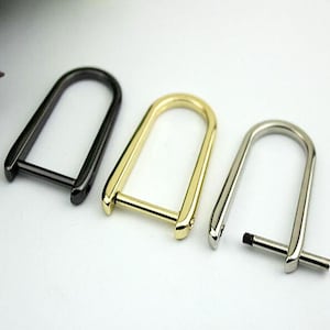 Puede incluir: Tres llaveros de metal en diferentes acabados: negro, dorado y plateado. Cada llavero tiene una abertura en forma de D y una barra recta que conecta los extremos.