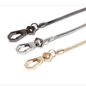 May include: Three chain straps with lobster clasps. The chains are silver, gold, and black.