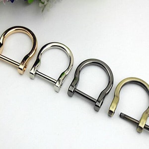 May include: Four metal D-rings in different finishes: gold, silver, black, and antique brass. Each ring has a screw closure.