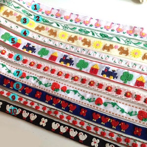 Könnte beinhalten: Zehn verschiedene bestickte Bandborten mit verschiedenen Designs, darunter Flamingos, Hunde, Häuser, Züge, Erdbeeren und Vögel. Die Bänder sind weiß mit bunter Stickerei.