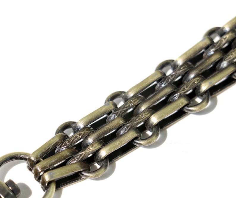 May include: A close-up of a gold-toned chain with a decorative pattern. The chain is made of multiple interwoven links.