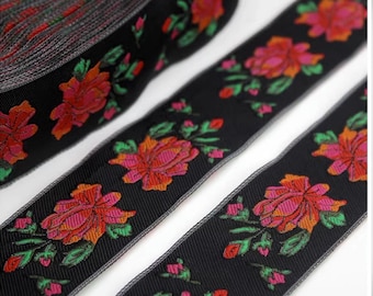 Puede incluir: Cinta negra de adorno con un patrón floral en tonos rosa, naranja y verde. La cinta tiene un brillo sutil y es perfecta para agregar un toque de elegancia a cualquier proyecto.
