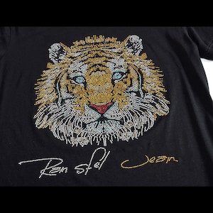 Può includere: Maglietta nera con un design a forma di tigre con strass e il testo "Ben-Shil" e "Jean" in strass dorati.