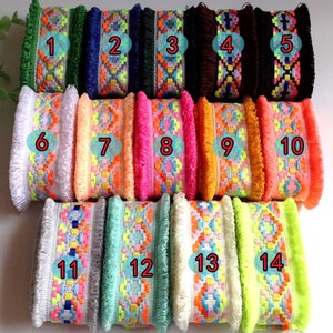 Peut inclure: Assortiment de 14 galons colorés avec franges. Le galon présente un motif géométrique avec différentes couleurs, notamment le rose, l'orange, le jaune, le vert, le bleu et le blanc. Le galon est numéroté de 1 à 14.