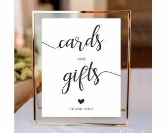 May include: A white sign with black calligraphy that reads "cards and gifts" with a small black heart below the text and "Thank You!" below the heart. The sign is in a gold frame.
