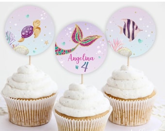 May include: Three cupcake toppers with a mermaid tail, a sea turtle, and a fish. The mermaid tail topper has pink and purple glitter and says "Angelina is 4".