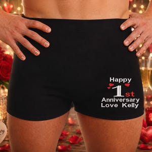 May include: Black boxer briefs featuring white text that reads Happy 1st Anniversary Love Kelly, with the number 1 in white and the letters st in red, accompanied by three small red heart icons positioned above the number 1 on the right side.