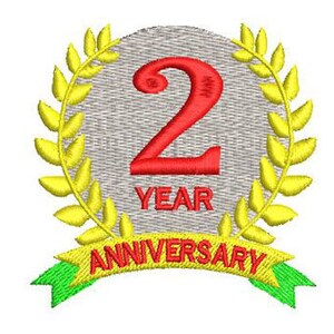 May include: A silver circle with a red number 2 and the text "2 YEAR ANNIVERSARY" surrounded by a yellow laurel wreath.