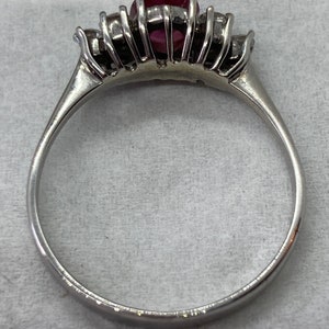 May include: A silver ring with a red gemstone surrounded by smaller clear gemstones.