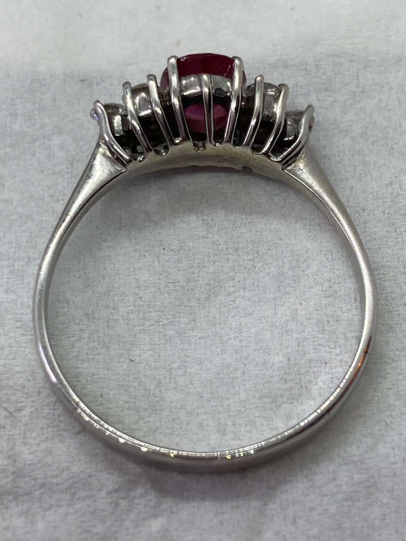 May include: A silver ring with a red gemstone surrounded by smaller clear gemstones.