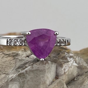 Könnte beinhalten: Ein silberner Ring mit einem dreieckigen violetten Edelstein und kleinen Diamanten auf der Ringschiene.